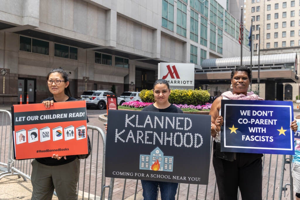 Protesters are seen with signs outside the Moms for Liberty summit in Philadelphia, one one that reads ''Klanned Karenhood'