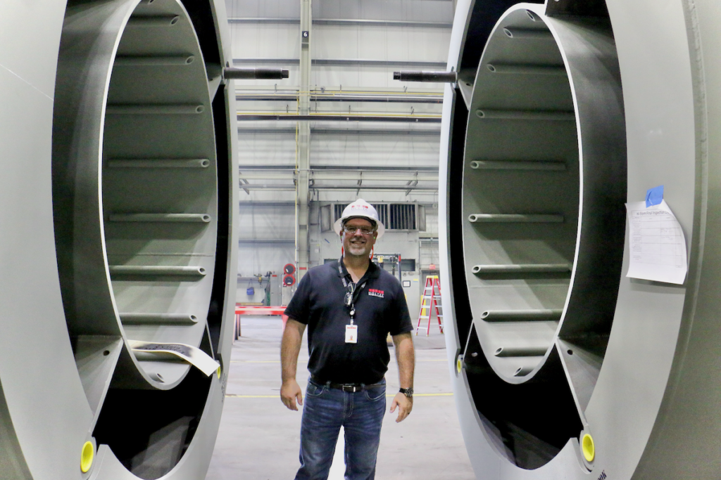 Derek Woodrum, Holtec's site safety representative, stands between two nuclear storage modules assembled at the company's manufacturing plant in Camden. (Emma Lee/WHYY)