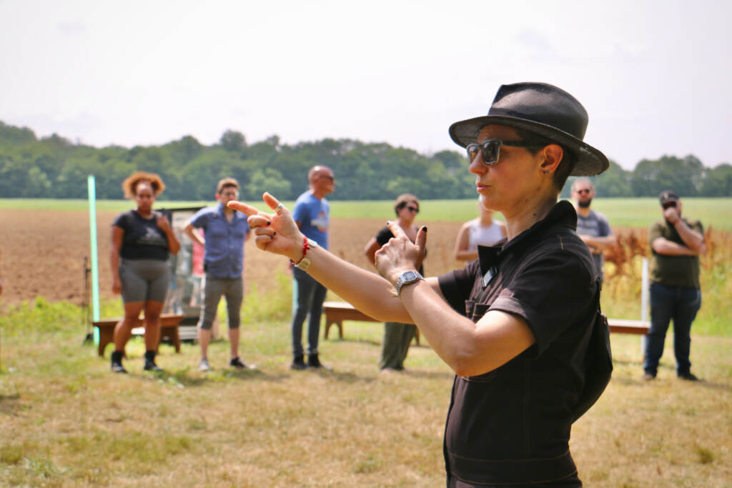 Ashley Tata gestures as she gives instructions to people gathered in an open field.