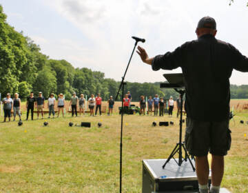 Donald Nally stands in front of a group of people, conducting the choir in an open field.