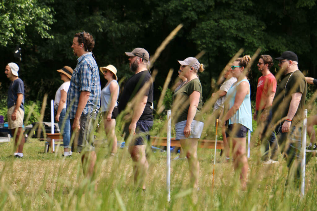 People stand in an open field during a rehearsal.