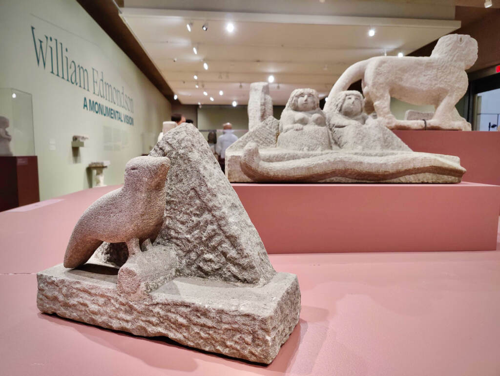 One sculpture shows a bird on a branch in the foreground. In the background is another sculpture, showing an ancient Egyptian couple.