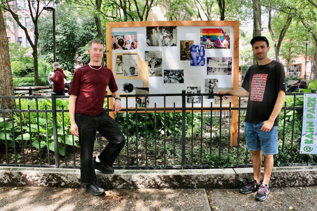 Jameson Paige, left, stands next to a board displaying photographs in a park with Rami George, right.