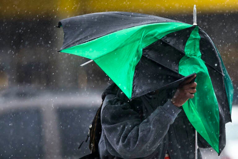 A pedestrian walks with little protection from his collapsed umbrella during a rainstorm