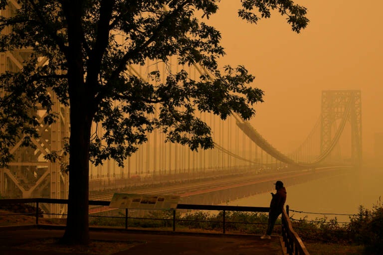 A man talks on his phone as he looks through the haze at the George Washington Bridge in Fort Lee, N.J., Wednesday, June 7, 2023. Intense Canadian wildfires are blanketing the northeastern U.S. in a dystopian haze, turning the air acrid, the sky yellowish gray and prompting warnings for vulnerable populations to stay inside