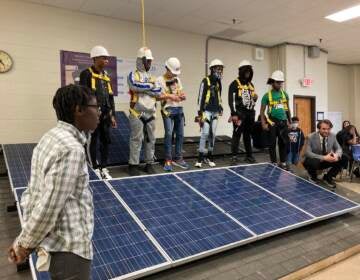 Anthony Cruz (back row, second student with hard hat from right), stands behind a solar panel with his classmates.