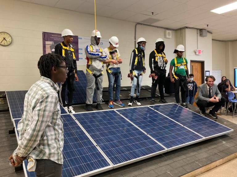 Anthony Cruz (back row, second student with hard hat from right), stands behind a solar panel with his classmates.