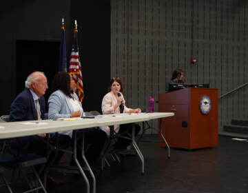 Three people sitting at a table on a stage addressing a crowd.