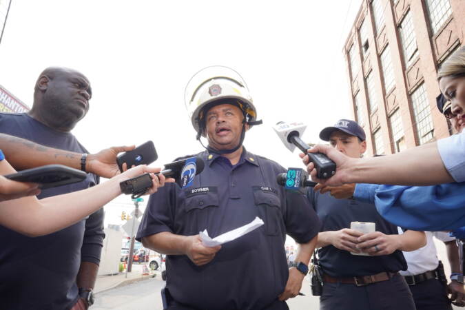 Philadelphia Fire Department Battalion Chief Derrick Bowmer, center, speaks with members of the news media, Sunday June 11, 2023, after a vehicle fire caused an overpass on I-95 to collapse near Cottman Avenue. (For WHYY/ Joseph Kaczmarek)
