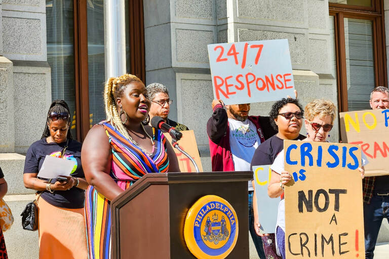 A woman speaks at a podium, with others holding signs next to her.