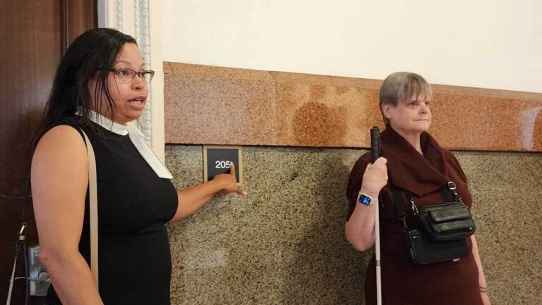 Adrienne Ewing and Susanne Erb stand beside a new ADA compliant sign in Philadelphia City Hall.