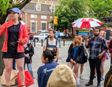 A guide speaks to a group of people gathered around her.