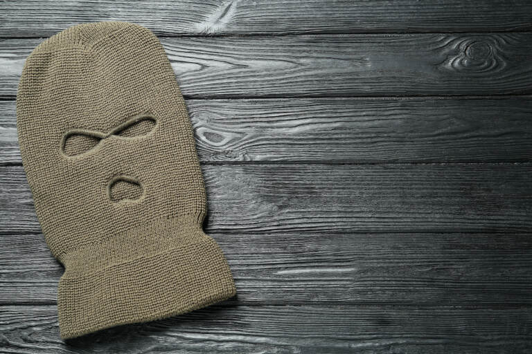 Beige knitted balaclava on black wooden table