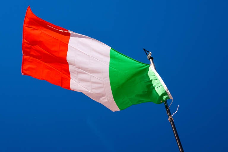 A view of an Italian flag waving in the wind with blue sky visible in the background.