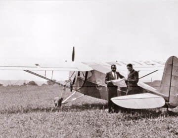 A black and white photo shows C. Alfred Anderson and Albert E. Forsythe next to an airplane.