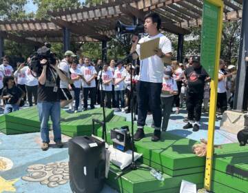 Wei Chen speaks into a megaphone in front of a crowd and members of the media.