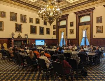 People sit in rows of chairs in a room at Philadelphia's City Hall.