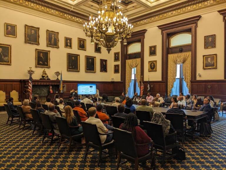 People sit in rows of chairs in a room at Philadelphia's City Hall.