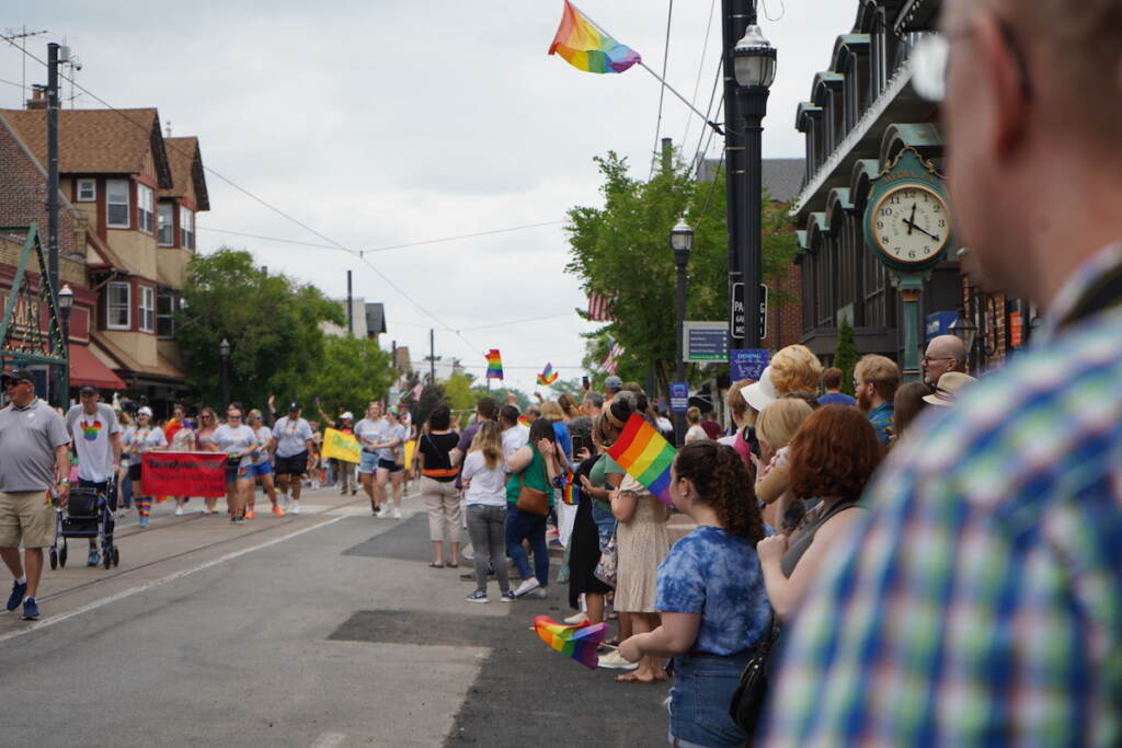 Spectators wave Pride flags as the Pride parade walks by them.