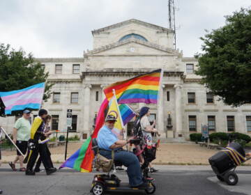 Pride participants pass in front of the Delaware County Courthouse, holding Pride flags.