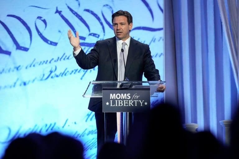 Ron DeSantis speaking at a podium at the Moms For Liberty conference