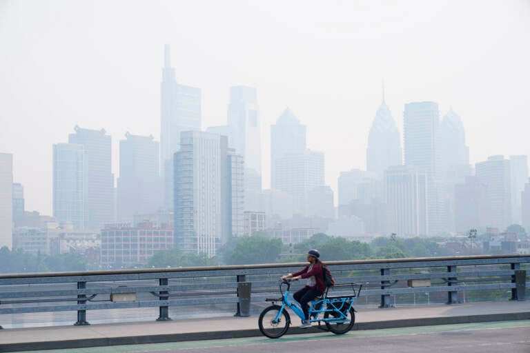 A person cycles past the skyline in Philadelphia shrouded in haze, Thursday, June 8, 2023.