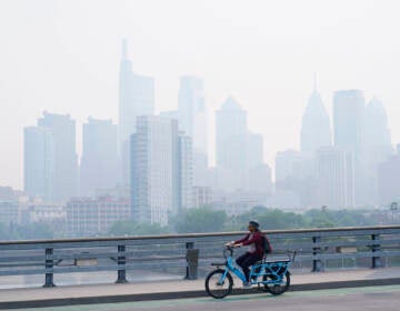 A person cycles past the Philadelphia skyline which is shrouded in a smoky haze.