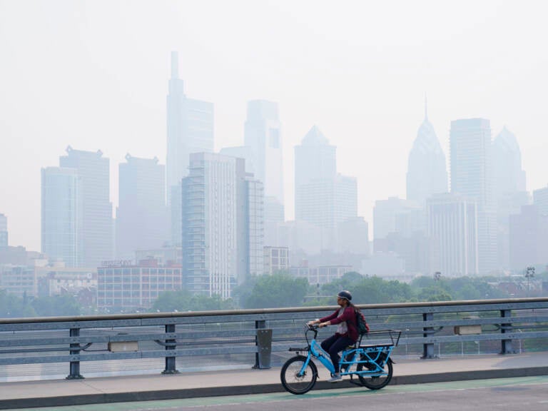 A person cycles past the Philadelphia skyline which is shrouded in a smoky haze.