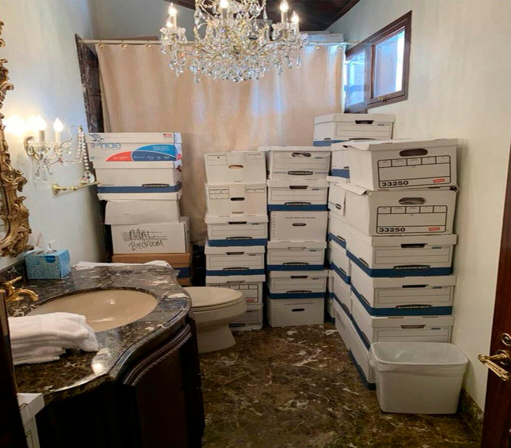 Stacks of boxes sit near the toilet in a bathroom.