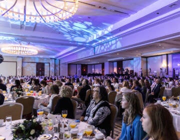 People are seated at round tables in a large conference room.