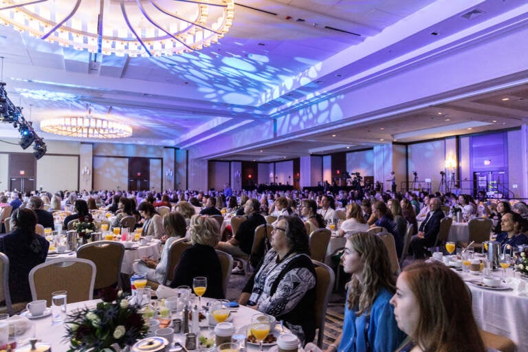 People are seated at round tables in a large conference room.