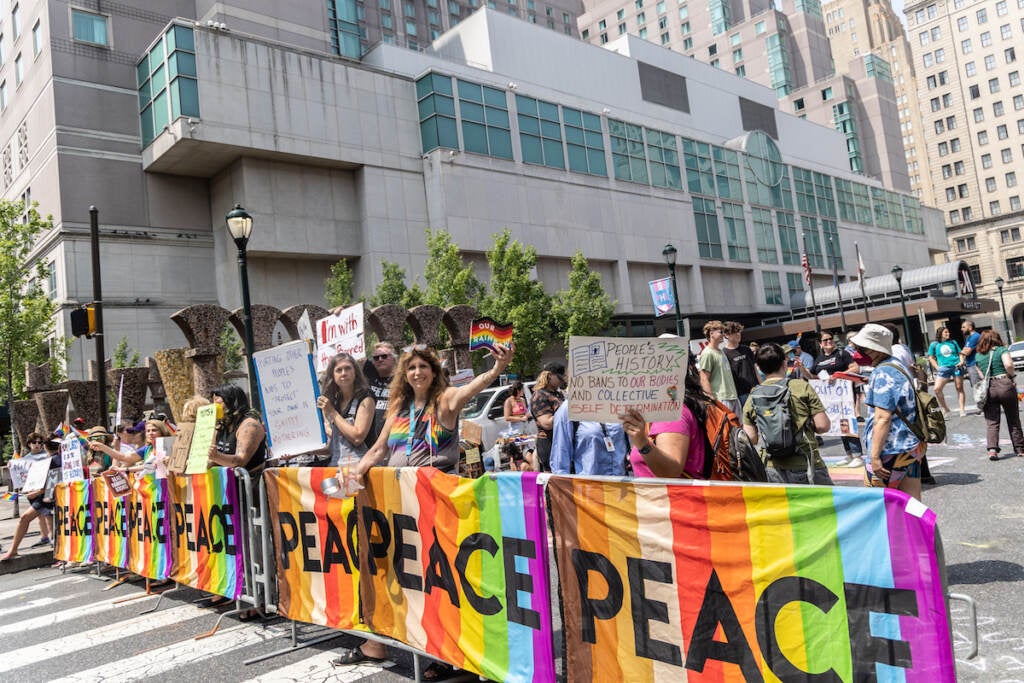 Protesters hold banners that are rainbow-colored with the word "Peace" printed on it.