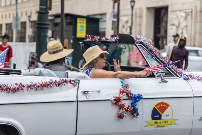 Two people ride in a Fourth of July decorated convertible.