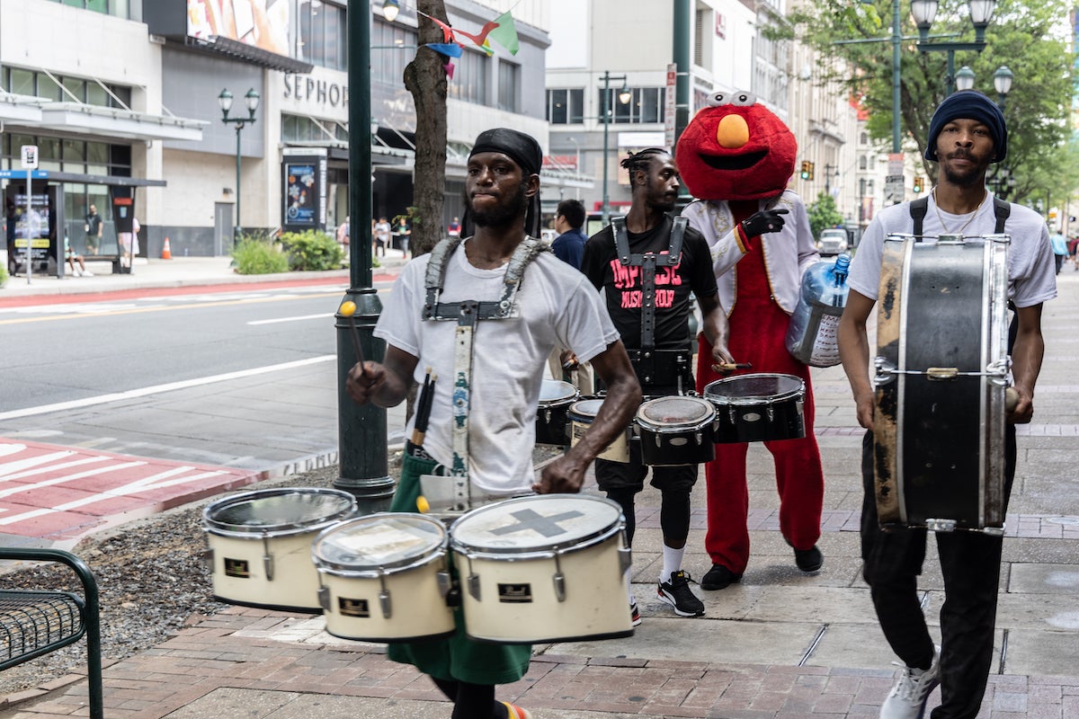 The Impulse Music Group drumline walks with someone dressed as Elmo