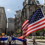 People carry the U.S. flag as they walk by City Hall in the Fourth of July parade.