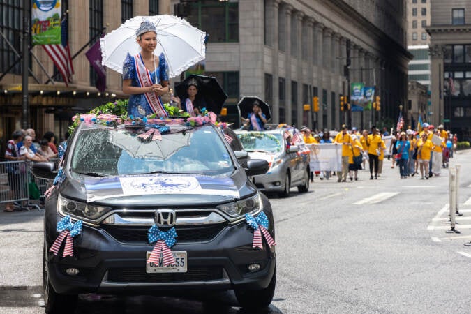 A beauty queen stands up and rides in a car in a parade.