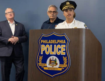 Commissioner Danielle Outlaw speaks at a podium. Mayor Jim Kenney and DA Larry Krasner look on behind her.