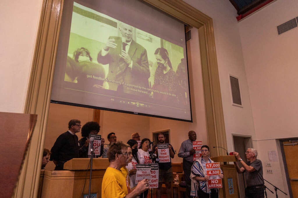 People gather at the front of a room. A projector shows a black-and-white photo.