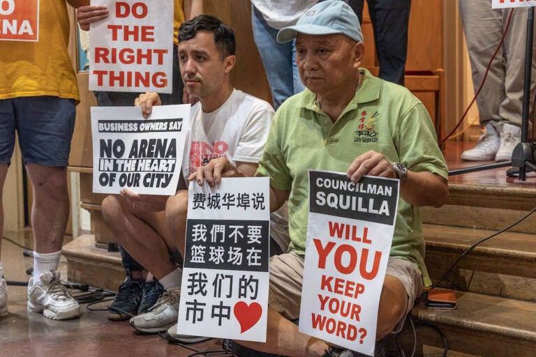 People hold signs that read Councilmember Squilla will you keep your word? Another person holds a sign written in Chinese.