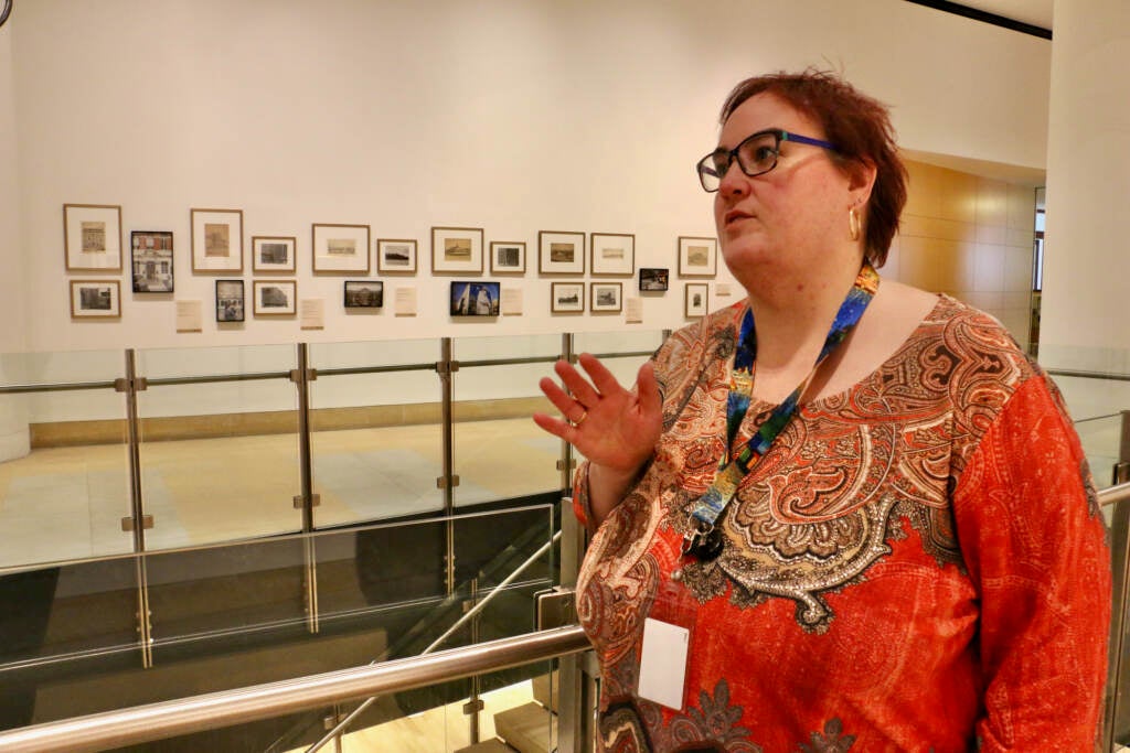 Stacey Swigart stands next to a row of paintings and photos that are part of a new exhibition.