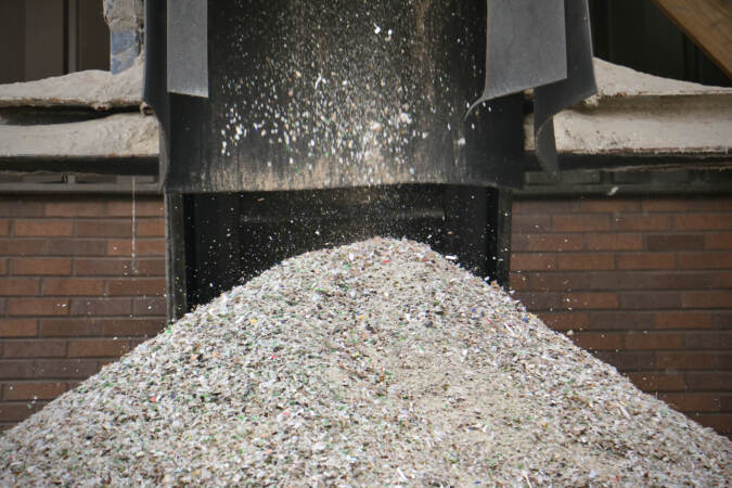A shower of crushed glass falls from a conveyor belt into a large pile.