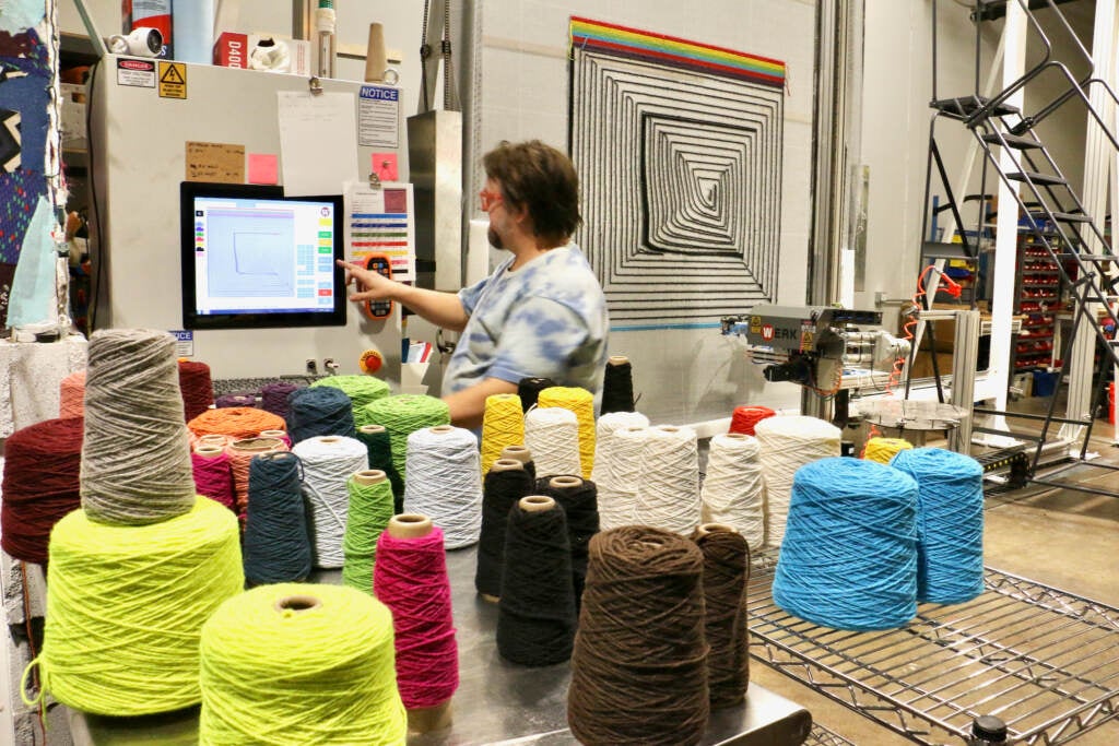 Tim Eads points to a screen in the background. In the foreground are spools of yarn.