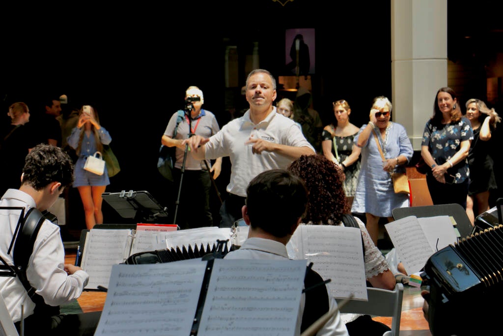 Frank Busso Jr. conducts the accordion orchestra playing at King of Prussia mall.