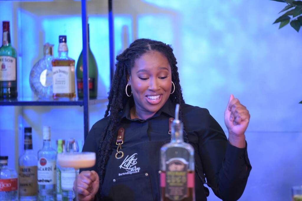 Khamila Barnes smiles while she mixes drinks at a bar.