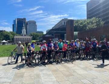 Cyclists pose for a photo in front of Independence Mall on a sunny day.