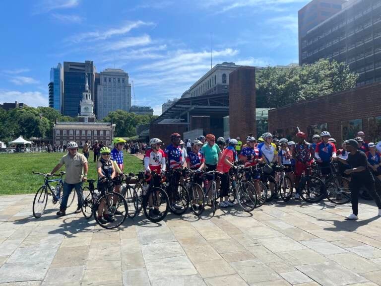 Cyclists pose for a photo in front of Independence Mall on a sunny day.