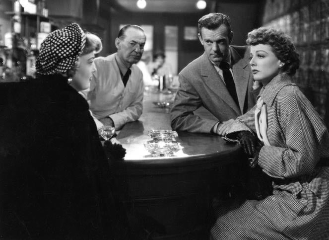 Ann Sheridan sits at a bar surrounded by other people in a black-and-white film still from the movie "Woman on the Run"