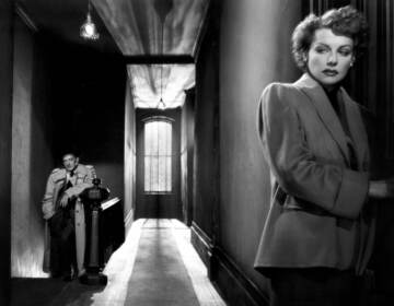 Ann Sheridan opens a door in a black-and-white film still as a man looks on in the background.