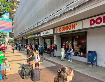 Passengers wait on a sidewalk for a bus