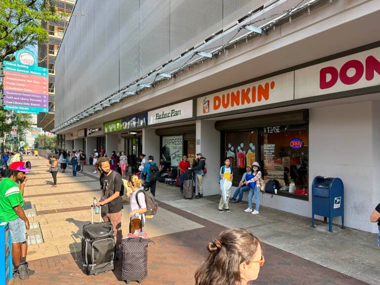 Passengers wait on a sidewalk for a bus